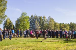 Silva metsänäyttelyssä yleisöä on kerääntynyt katsomaan tukkilaisten esitystä. Keskellä kaksi tukkilaisasuihin pukeutunutta miestä valmistelee tukkeja. 