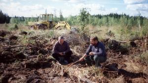 Kaksi ihmistä tarkastelemassa maanmuokkausaluetta.