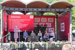 Juontaja ja paneelikeskustelijat SuomiAreenan lavalla.