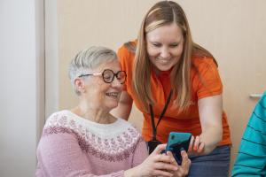 Skogscentralens rådgivare tittar tillsammans med en äldre kvinna på uppgifter på mobiltelefonens skärm.