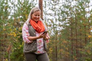En person tittar på en mobiltelefon och ler medan hen går i skogen.
