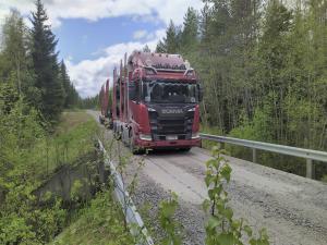 En virkestransportbil på en bro på en skogsväg på sommaren.