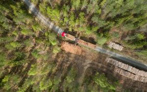 Ylhäältä päin kuvattuna tukkirekka metsätiellä ja puupinoja. 