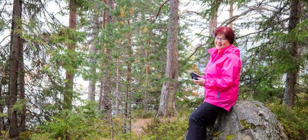 Metsänomistaja istuu kivellä metsässä kädessään tablettitietokone.