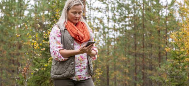 En person tittar på en mobiltelefon medan hen går i skogen.