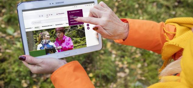 Henkilö pitää kädessään tablettia ja osoittaa ruudulta Metsäkeskuksen verkkosivujen Metsään.fi-palveluun kirjautumiskohtaa.