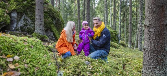 Kaksi aikuista ja lapsi kävelemässä metsässä.