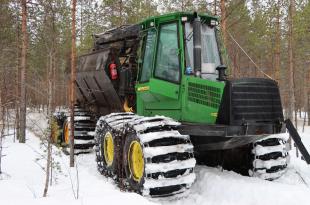 Metsätraktori tekemässä lannoitusta talvisessa metsässä. 