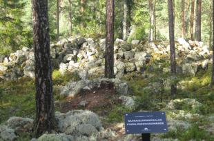 Muinaisjäännösalue metsän keskellä, taustalla on kiviä suuressa pinossa.