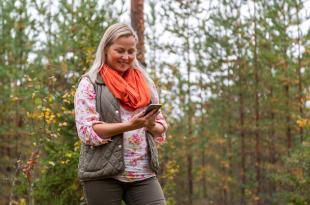 En person tittar på en mobiltelefon och ler medan hen går i skogen.