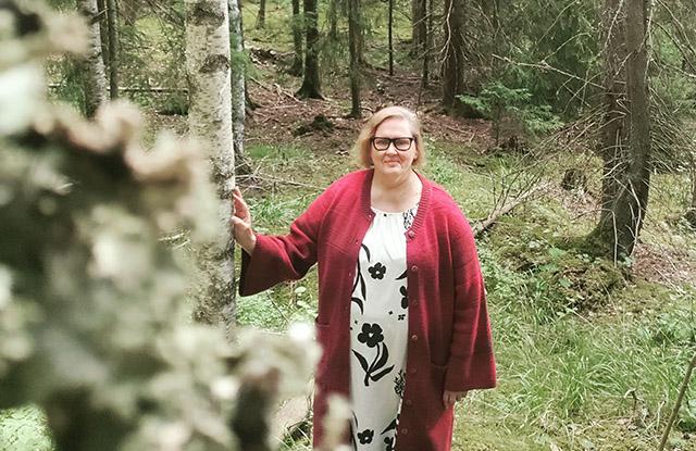Nainen seisoo sekametsässä ja katsoo kameraan.