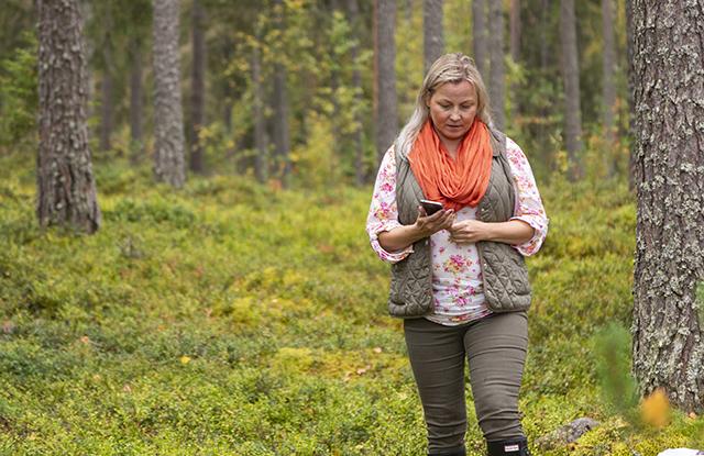 Nainen kävelee metsässä ja katsoo puhelintaan.