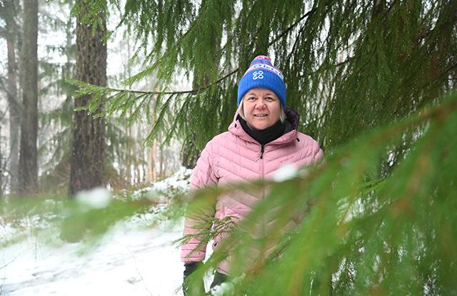 Nainen metsässä kuusen oksien katveessa.
