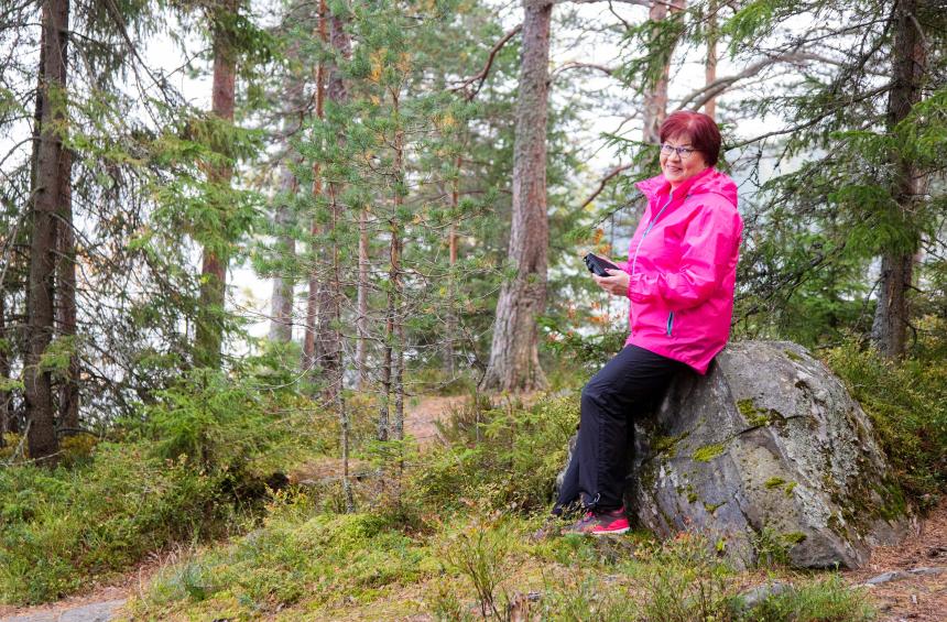  En skogsägare sitter på en sten i skogen och håller i en surfplatta.